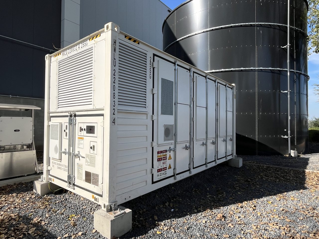 Containerised battery storage unit beside industrial storage tanks